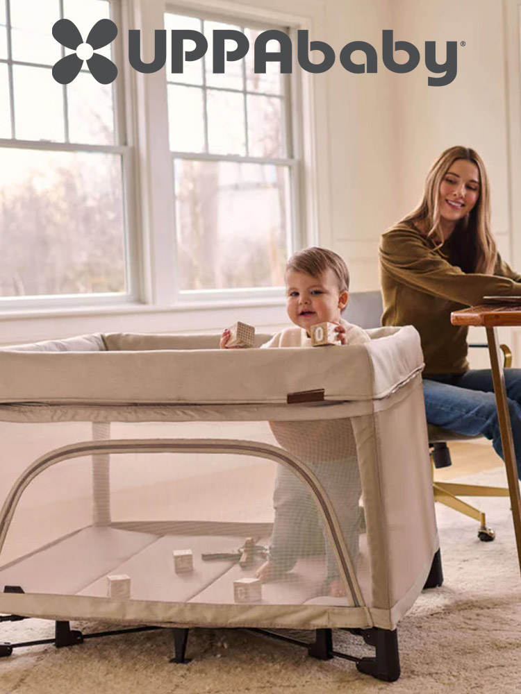 a toddler standing and playing in the uppababy remi playard travel crib