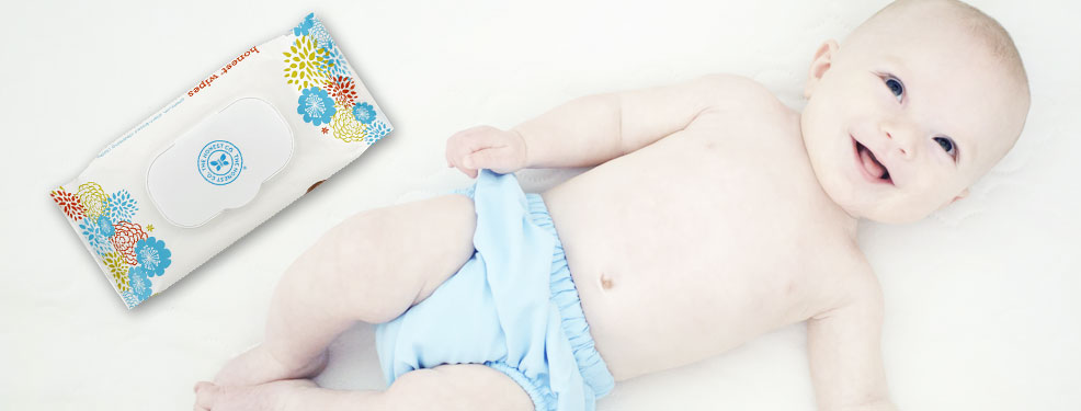 a smiling baby laying next to a pack of baby wipes