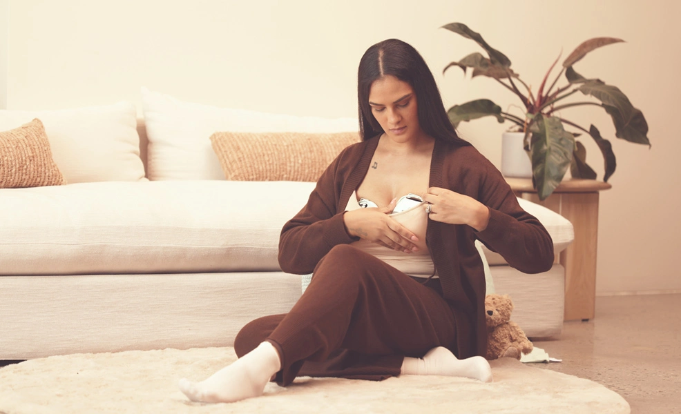a woman sitting in her living room using the zomee w1 breast pump warming wearable